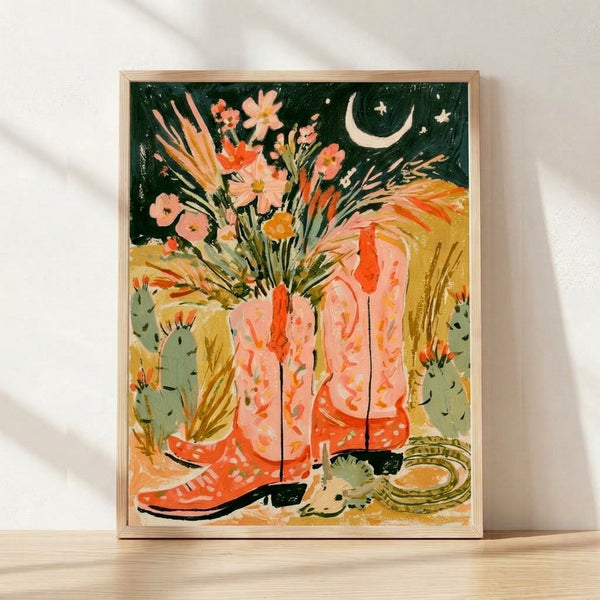 Watercolor boho art print featuring cowboy boots filled with desert flowers, cacti, and a crescent moon in warm terracotta, coral pink, sage green, and teal tones on a framed poster.