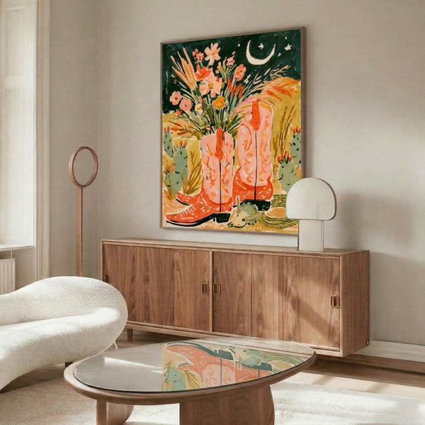 Modern boho wall decor featuring a watercolor scene of cowboy boots overflowing with flowers and moonlit desert botanicals in warm peachy and sage green hues.