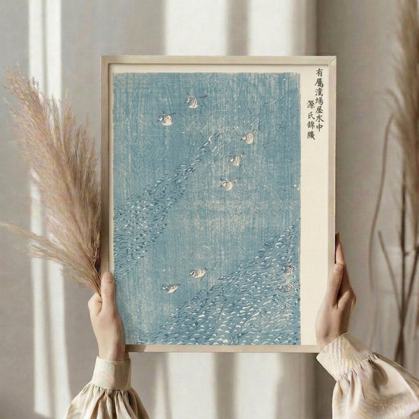 Traditional Japanese woodblock poster showing birds in a rocky stream, muted color palette of pale blue and charcoal conveying tranquil mood.