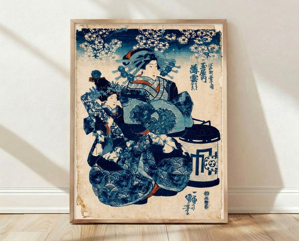 Framed Japanese woodblock print depicting an elegant geisha in a deep indigo kimono with coral red accents, attended by a young child, surrounded by delicate cherry blossoms and a lantern in soft palette tones.