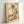 Traditional Japanese woodblock artwork featuring a graceful figure in an elaborately decorated kimono, rendered in soft cream, coral, and olive tones with ornamental botanical elements.