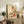 Serene Japanese art print portraying a geisha amid decorative floral arrangements, her kimono rendered in refined coral and olive hues with ornamental detail work throughout.
