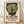 Art Deco framed poster of an ancient Mexican mosaic mask with geometric beading and necklace in sage green, rust orange, and charcoal black on cream background.