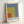 Bauhaus-style framed artwork showing clean geometric abstraction with distinct color fields in slate, rust, yellow, and cream arranged in disciplined rectangular forms.