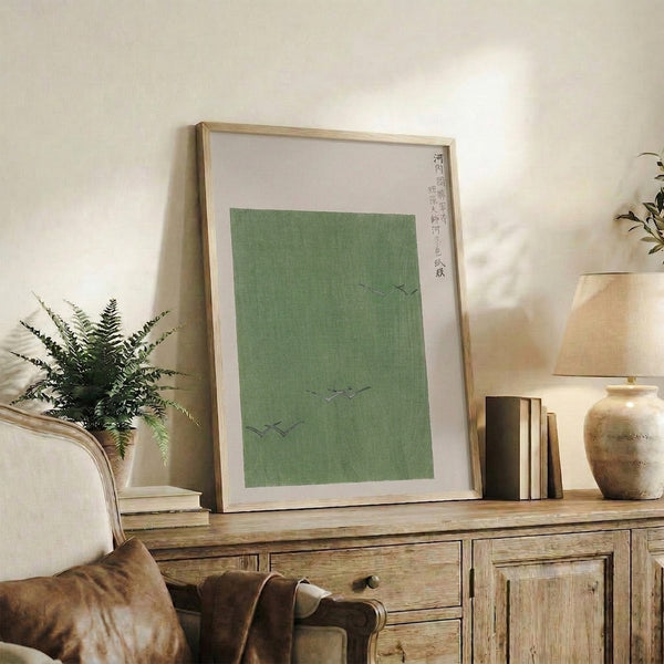 Contemplative woodblock-style poster of birds and temple landscape in restrained sage green, cream, and charcoal, hung as framed wall decor.