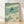 Minimalist Japanese woodblock-style poster depicting a graceful swallow in flight against a soft sage green sky, with serene waves in cream and teal tones below.