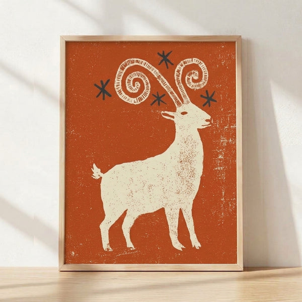 Framed folk art poster featuring a whimsical ibex goat with curved horns and a cream-colored star, rendered in rust orange, navy blue, and speckled textures in retro boho style.