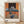Abstract modern poster featuring a distorted figure seated at a table with a stark light bulb, rendered in burnt orange, dark brown, and slate blue tones that evoke an unsettling, introspective mood.