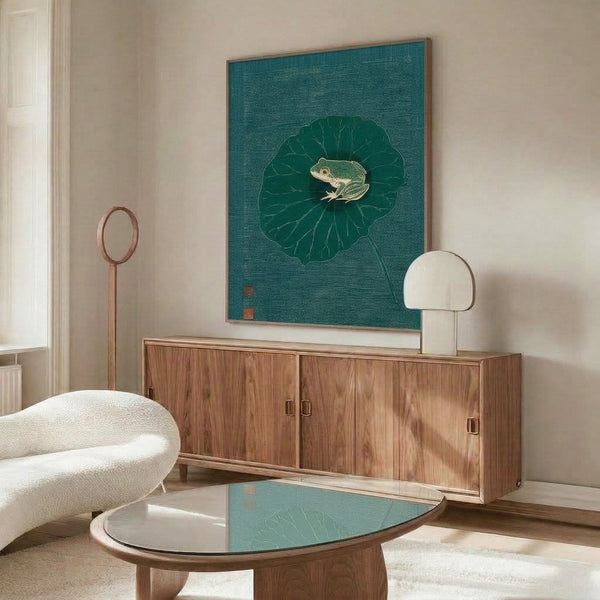 Framed wall art showing a naturalistic Japanese woodblock composition of a frog resting on a lotus leaf, executed in delicate line work with serene forest green and teal coloring.