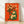 Retro folk art poster of a cheerful frog holding a daisy bouquet in burnt orange, cream, and forest green tones, framed on a wall.