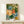 Warm, cozy watercolor composition of a tea service with pottery vessels, blooming florals, and botanical elements in soft sage, cobalt blue, and golden hues, displayed as framed wall art with domestic charm.