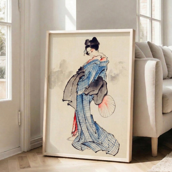 Framed traditional ukiyo-e print showing an elegant geisha in a blue geometric kimono with fan, rendered in cream, coral pink, and black with timeless serene beauty.