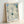 Framed poster displaying a delicate cream-colored flower with layered petals in muted teal and pale blue hues, evoking a calm and introspective mood through minimalist abstraction.
