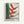 Bold modernist botanical poster featuring a close-up heliconia bloom in rich crimson and emerald tones with sky blue sky, framed in a contemporary interior.