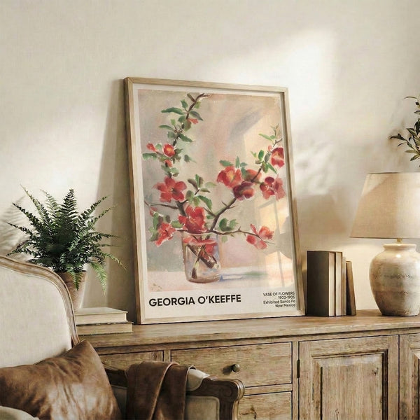 Framed watercolor botanical poster inspired by O'Keeffe, showing red blooms and green foliage in a cream vase with warm earthy undertones throughout.