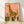 Minimalist watercolor giraffe in coral pink and golden yellow tones, surrounded by savanna grasses and plants in olive green, framed poster on wall creating a calm, whimsical atmosphere.