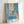 Framed impressionist wall art depicting an intimate domestic scene: goldfish bowl, blooming flowers, reclining woman, and sculpture in harmonious palette of blue and pink hues.