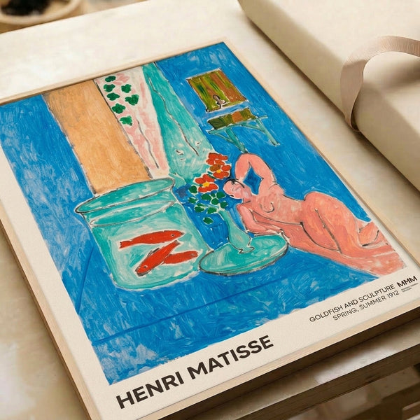 Matisse's 1912 composition as a framed print—serene arrangement of goldfish, woman, flowers, and sculpture unified by soft blue-green and rust-accented impressionist palette.