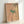 Delicate framed poster depicting a bird on a blossoming branch in muted peach and sage green, rendered in serene Japanese woodblock style.