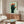 Framed minimalist Bauhaus-inspired artwork showing a conceptual hand design with five faces integrated into the composition, palette of sage green, burnt orange, and cream.