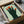 Contemporary poster art with a geometric hand and five faces in surreal arrangement, Bauhaus design sensibility, muted sage and forest green with burnt orange accents.