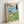 Studio Ghibli wall art depicting a gentle forest spirit among blooming grass and flowers, holding an umbrella, with a nostalgic and dreamlike quality in soft pastel colors.