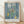 Matisse's The Blue Window, a serene modern interior scene featuring a vase of flowers and potted plant on a table, rendered in soft teal blue, pale yellow, and sage green tones.