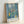 The Blue Window by Henri Matisse, a light-filled composition with bottles, flowers, and plants arranged on a table, executed in muted palette of navy, cream, and soft greens.