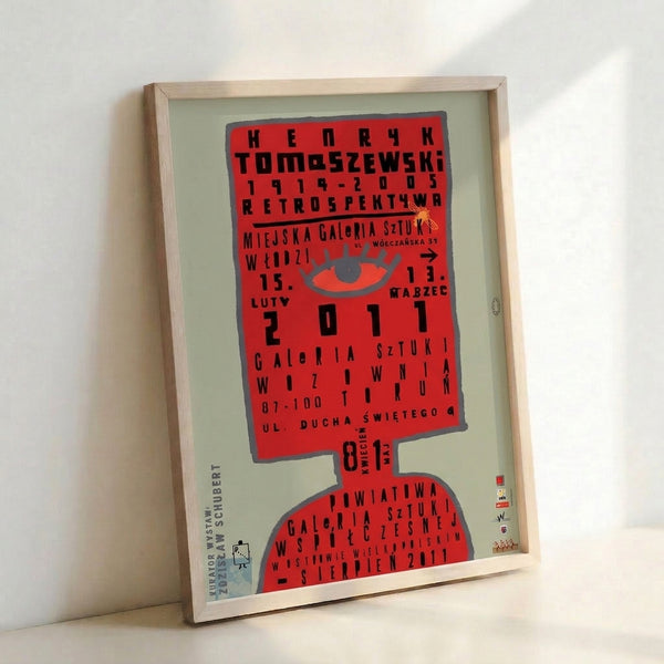 Framed minimalist poster displaying an abstract eye in red-orange with stark black lettering, embodying the graphic boldness of Bauhaus design.