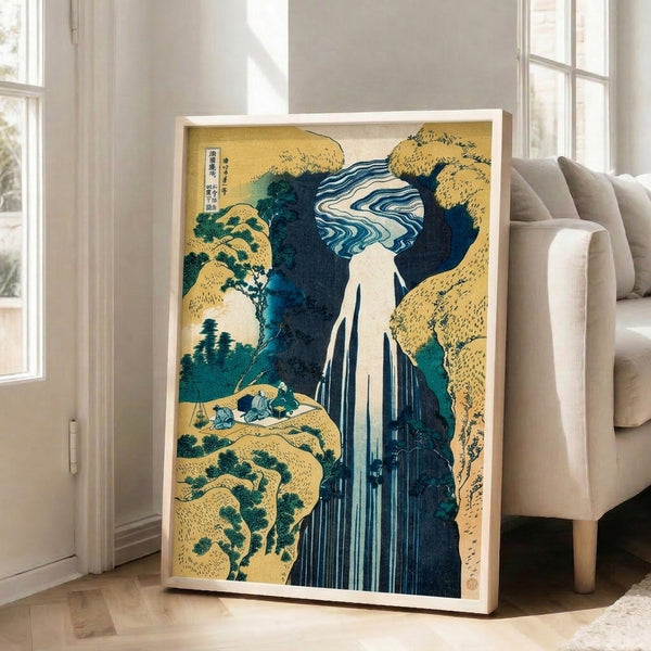 Traditional Japanese woodblock art print portraying a waterfall scene with rocky formations and distant mountains; calming color palette of indigo, green, and cream on display as framed wall art.