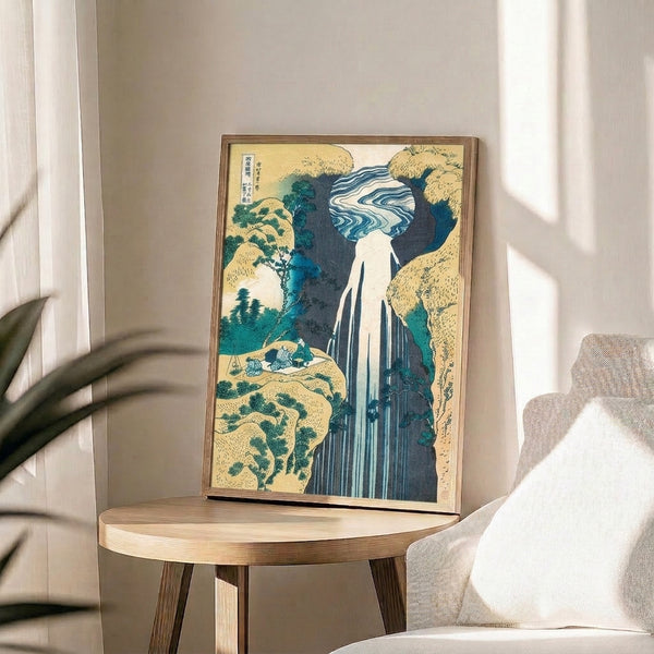 Framed vintage Japanese art print showcasing a tall waterfall amid towering cliffs and forest; serene composition in tones of deep indigo, teal, and pale ochre.
