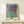Monet-inspired garden art print displaying a contemplative scene of a dwelling amid abundant flowering roses in gentle rose pink and green palette.
