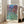 Serene impressionist watercolor poster featuring a house nestled within blooming roses and garden foliage in soft cream, blue, and violet tones.