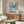 Wall art poster presenting a dreamlike Ghibli-inspired castle scene nestled among fluffy clouds with pastoral elements and mountain silhouettes in calming sky blue and cream tones.
