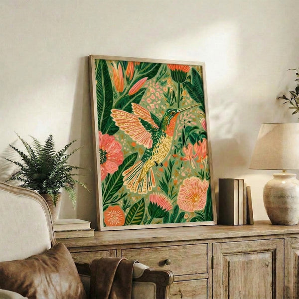 Whimsical watercolor painting of a hummingbird surrounded by lush forest green foliage and delicate blooms in soft sage and coral tones, displayed as a framed poster.
