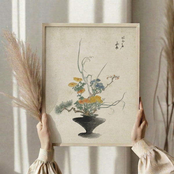 Contemplative Japandi art print of a traditional ikebana composition with delicate chrysanthemum blooms in warm ochre tones, graceful leafy stems in muted sage, and charcoal linework on cream background, displayed as framed wall art.