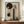 May include: Framed abstract art print featuring dark green circles and geometric shapes with misty tree silhouettes, displayed on wooden sideboard next to white ribbed vase and stack of books in neutral-toned room with cream walls and decorative molding.