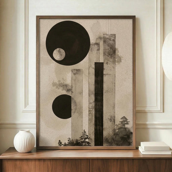 May include: Framed abstract art print featuring dark green circles and geometric shapes with misty tree silhouettes, displayed on wooden sideboard next to white ribbed vase and stack of books in neutral-toned room with cream walls and decorative molding.