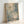 Abstract expressionist artwork in light wooden frame leaning against white wall. Soft blue, green, and cream paint splatters blend with delicate white dots and thin crossing lines throughout. The dreamy, ethereal composition has a watercolor-like quality with organic paint drips and gentle color transitions creating a peaceful, contemporary aesthetic.