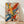 May include: Vibrant abstract expressionist artwork with energetic paint splatters and bold brushstrokes in yellow, blue, red, and orange displayed in a thin wooden frame, leaning against a white wall on light wood flooring with natural window light creating soft shadows