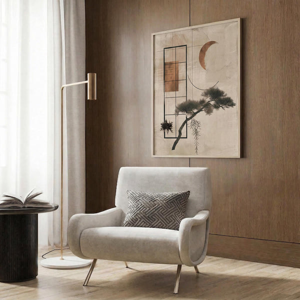 May include: Abstract artwork displaying geometric rectangles, crescent moon, and stylized pine tree with drooping branches in earth tones, mounted on wood-paneled wall above beige upholstered armchair with geometric patterned pillow, brass floor lamp, and dark round side table with open book in modern neutral living room setting.