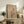 May include: Framed minimalist poster featuring a bare black tree silhouette against a beige background with geometric shapes including a red circle, large tan circle, and organic flowing forms. The artwork is displayed on a rustic wooden console beside a fern plant, pottery vase, books, and brown leather chair in a neutral-toned living room setting.