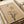 May include: Minimalist art print displayed in an open book or portfolio, featuring a bare black tree silhouette against a warm beige background with geometric shapes - a small red-orange circle, thin red lines, and soft brown oval forms suggesting sun and abstract elements. The print has a clean modern aesthetic with neutral earth tones.