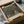 May include: Gustav Klimt art print in wooden frame being unpacked from cardboard box with tissue paper. The artwork shows a tree-lined path leading to a yellow building, painted in earthy greens and browns with Klimt's distinctive style. Museum of Modern Art New York attribution visible at bottom. Frame sits among white tissue paper with wooden corner protectors.