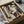 May include: Art deco style portrait poster in black frame being unpacked from cardboard shipping box with tissue paper. Abstract geometric woman's face in earth tones - beige, brown, olive green, rust orange. Minimalist cubist design with flowing hair and stylized features. Frame appears medium-sized next to wooden dowel rods and glass container in background.