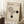 May include: Framed Bauhaus-inspired poster with geometric design featuring curved lines forming abstract shapes and two black circles on cream textured background, displayed in bright room corner with coffee cup on wooden block and cozy blanket nearby