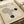 May include: Vintage-style cream poster with "BAUHAUS 1919" header featuring geometric line art design with curved and straight parallel lines forming an abstract shape, accompanied by two dark green circular elements. German text appears at bottom. Poster shown on beige surface with white paper rolls in background, creating a minimalist workspace setting.