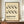 May include: Framed beige poster with black wavy geometric pattern and "BAUHAUS" text, displayed on wooden sideboard next to white ceramic vase and stacked books against cream paneled wall in modern interior setting