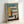Framed architectural poster featuring geometric Bauhaus-style building illustration in teal, yellow, coral, and cream colors. Modern minimalist design shows abstract building forms with horizontal lines and rectangular shapes. White "02" visible on left side, "Form Follows Function" text at bottom. Light wood frame, leaning against white wall on white surface.