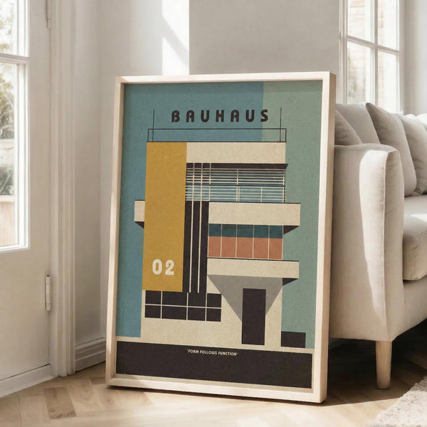 May include: Framed Bauhaus-inspired architectural poster showing geometric building design with yellow, teal, coral and cream colored blocks, displayed on wooden floor next to beige upholstered chair in bright room with white walls and windows.